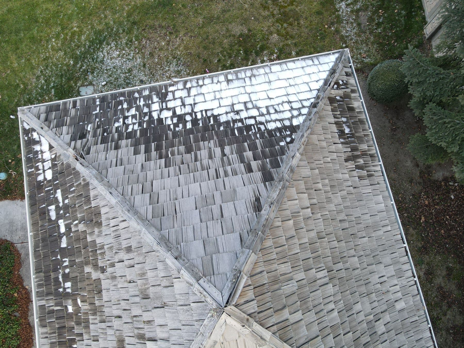 Drone view of a worn cedar shake roof with the first snow sitting in patches