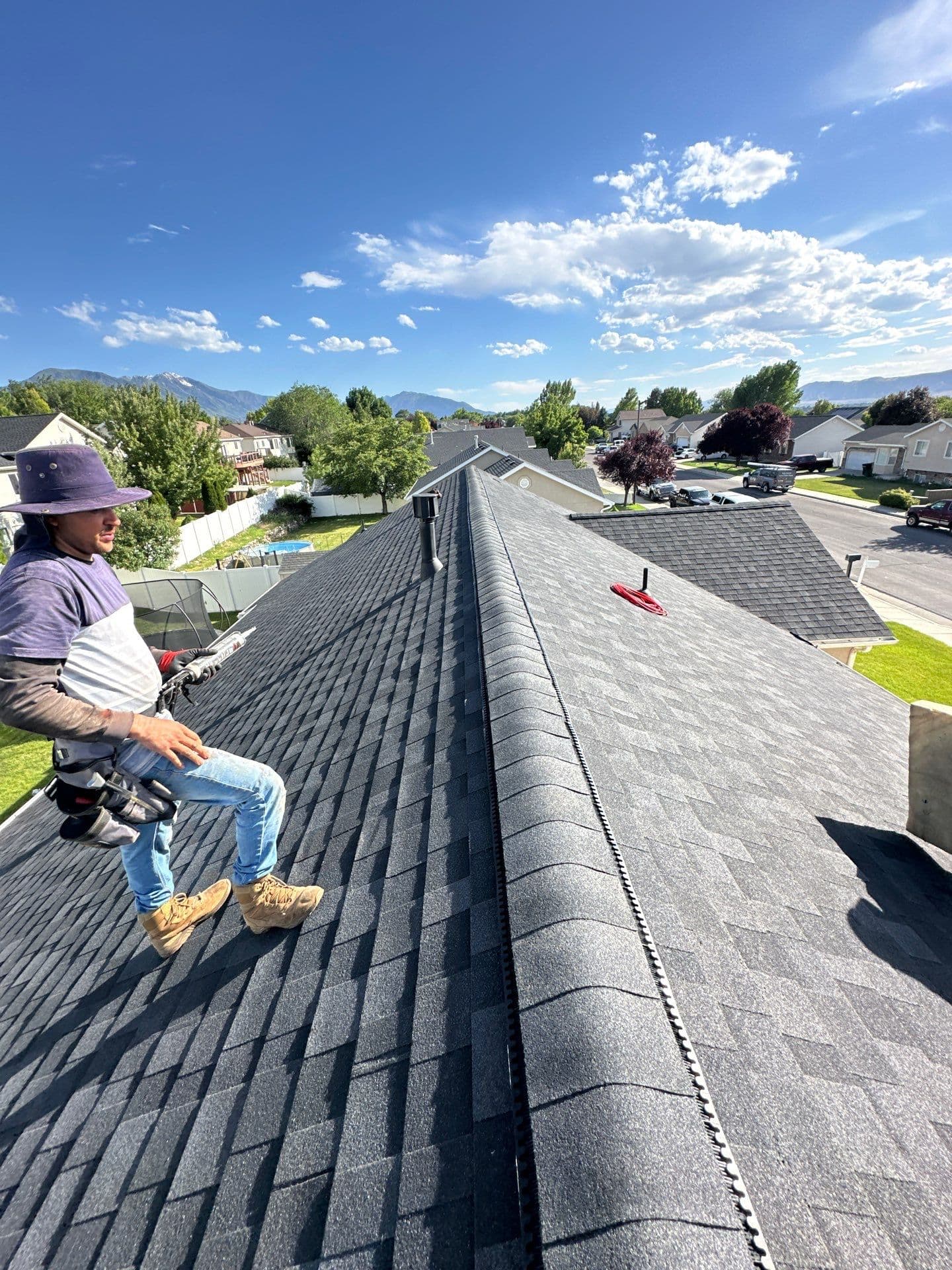A Robinhood crew member on a finished roof above a Utah neighborhood, mountains behind