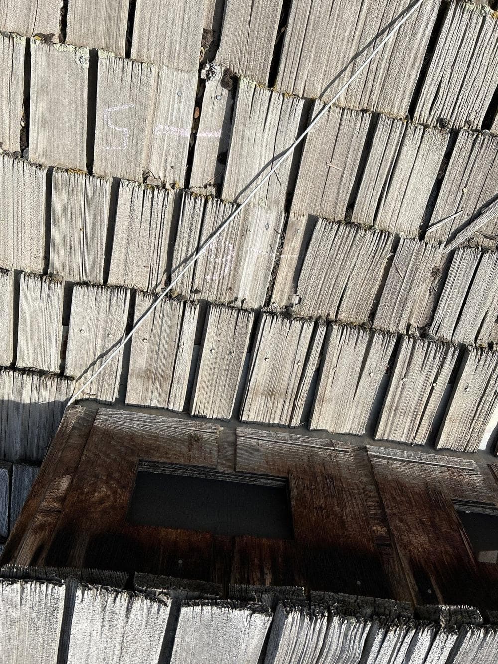 Split and eroded cedar shake beside an old skylight
